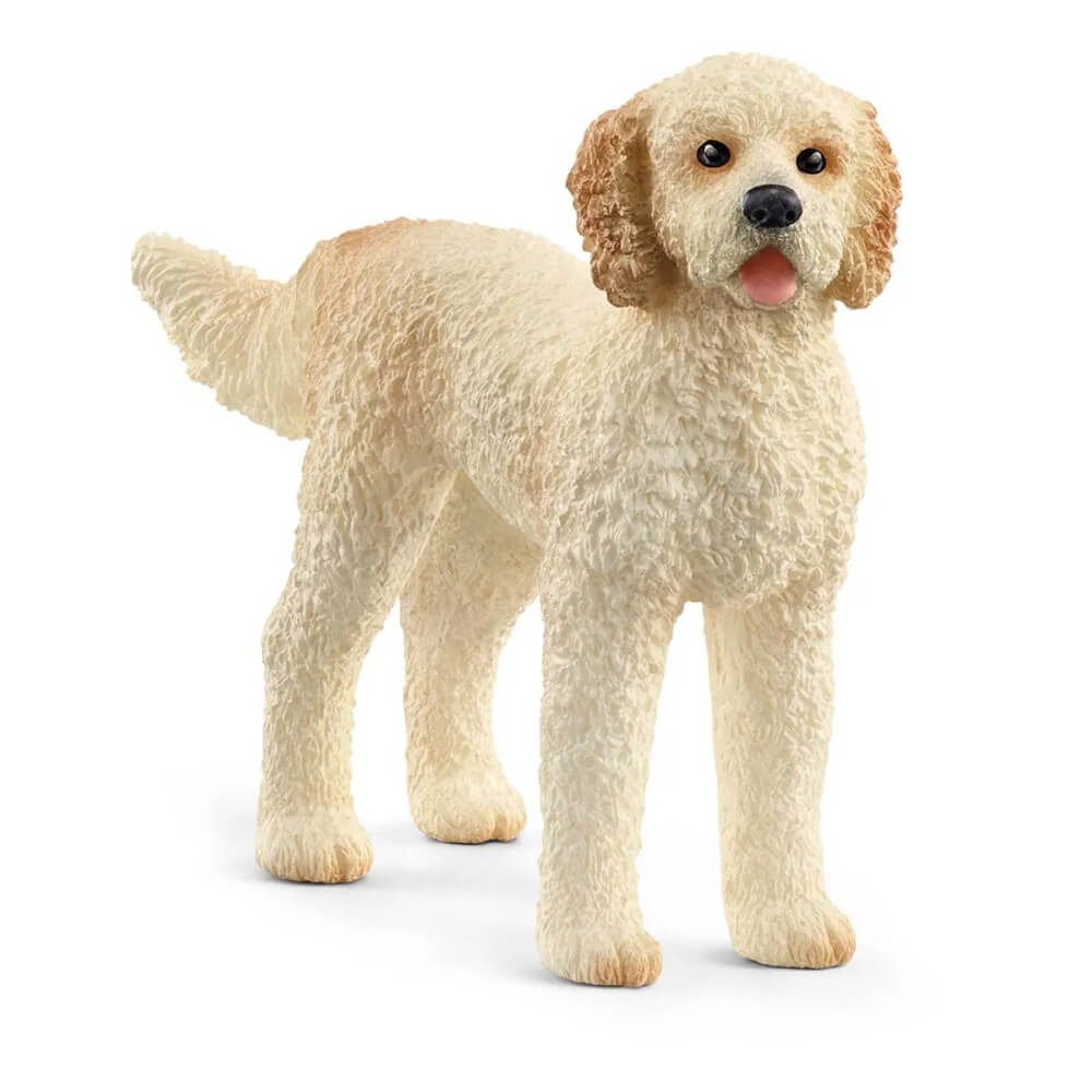 Cream and light tan Schleich Farm World Goldendoodle dog figurine features textured curly fur, floppy ears, a raised tail, black eyes and nose, and a pink tongue, standing on a white background.